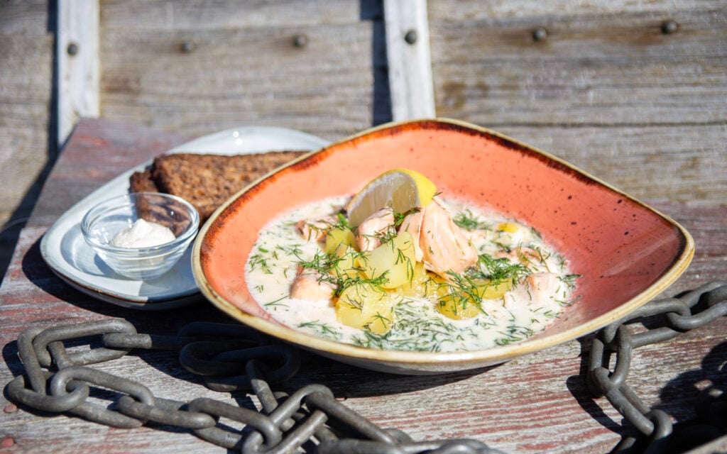 Kesäinen ja aurinkoinen sää, vanhassa veneessä on aseteltuna lohikeittolautanen ja vieressä saaristolaisleipää