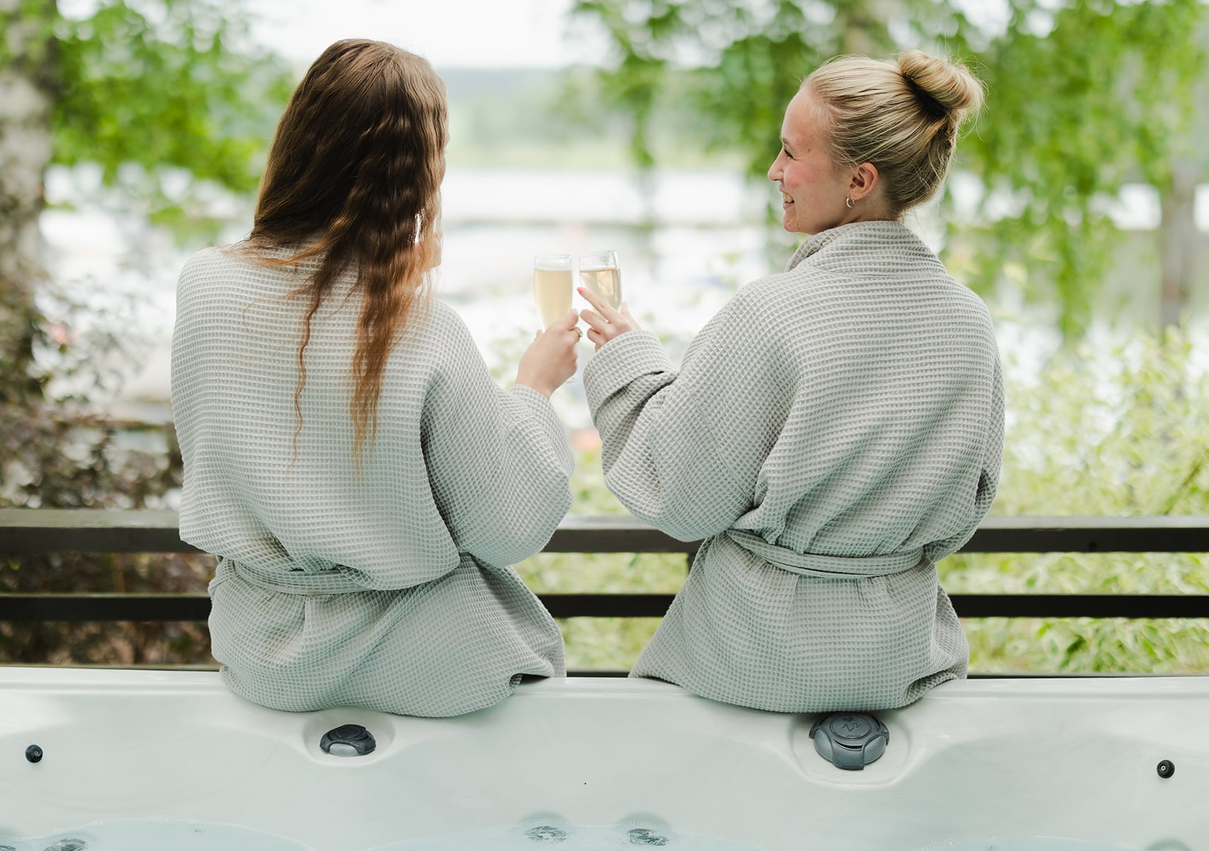 Kaksi naista skoolaavat ulkoporealtaan reunalla istune, taustalla näkyy kesäinen satama ja merimaisema